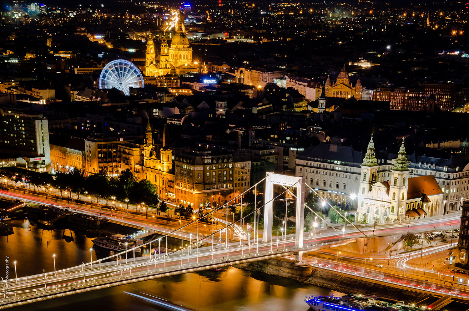The Elisabeth Bridge illuminated in white light at night. In the background is the St. Stephen's Basilica.
