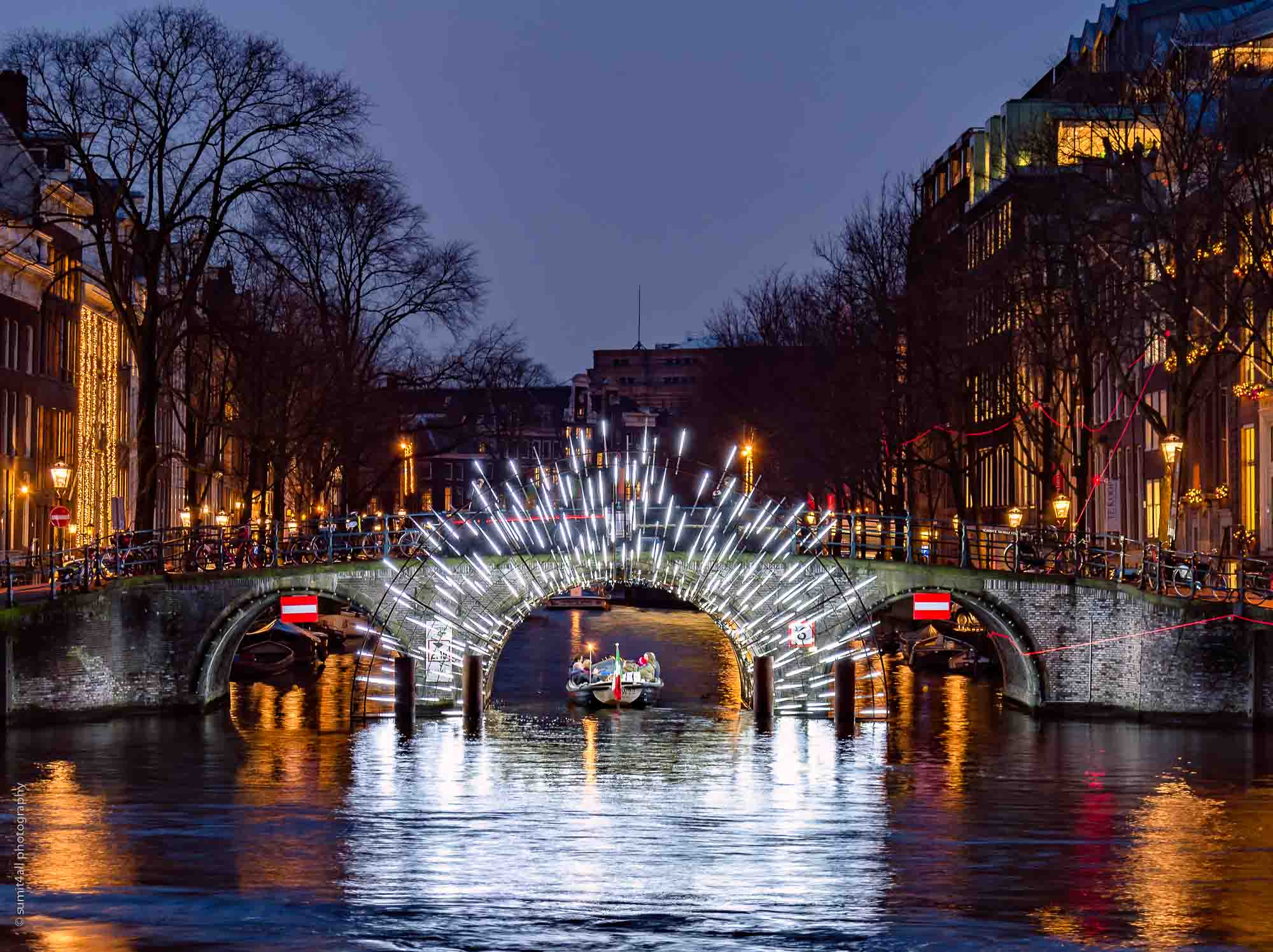 Boat passing under a light artwork on a bridge during the Amsterdam Light Festival