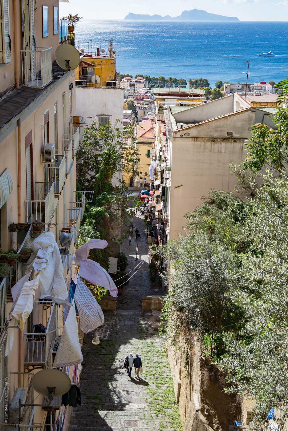 A hilly street sloping down in Naples and the Isle of Capri in the Background