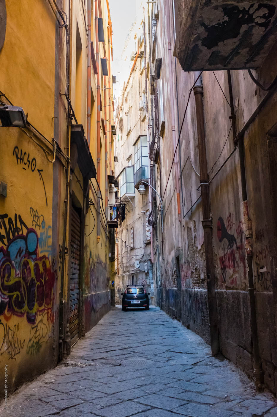 A car passes through a narrow road in Naples, Italy